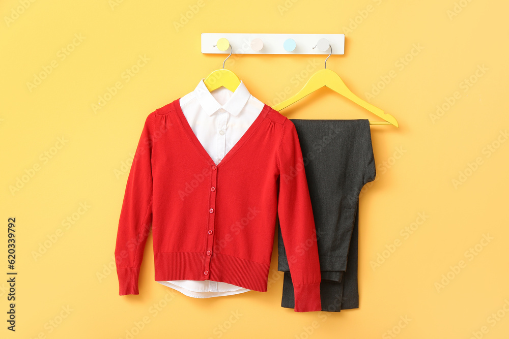 Stylish school uniform hanging on rack against yellow wall