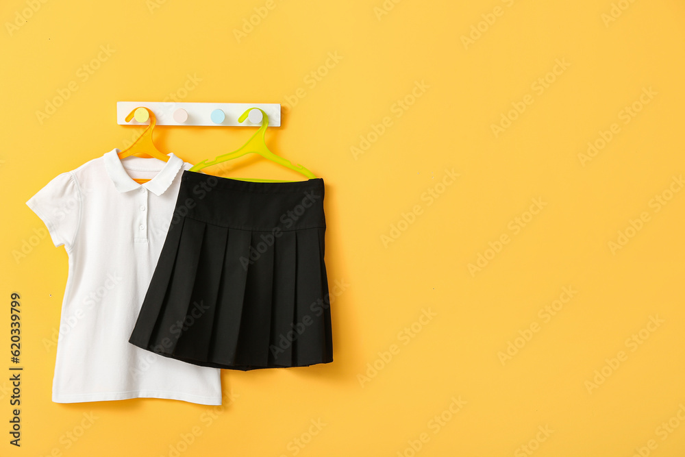 Stylish school uniform hanging on rack against yellow wall