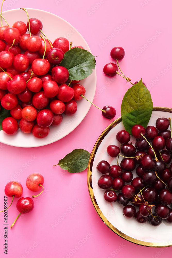 Plates with sweet cherries and leaves on pink background