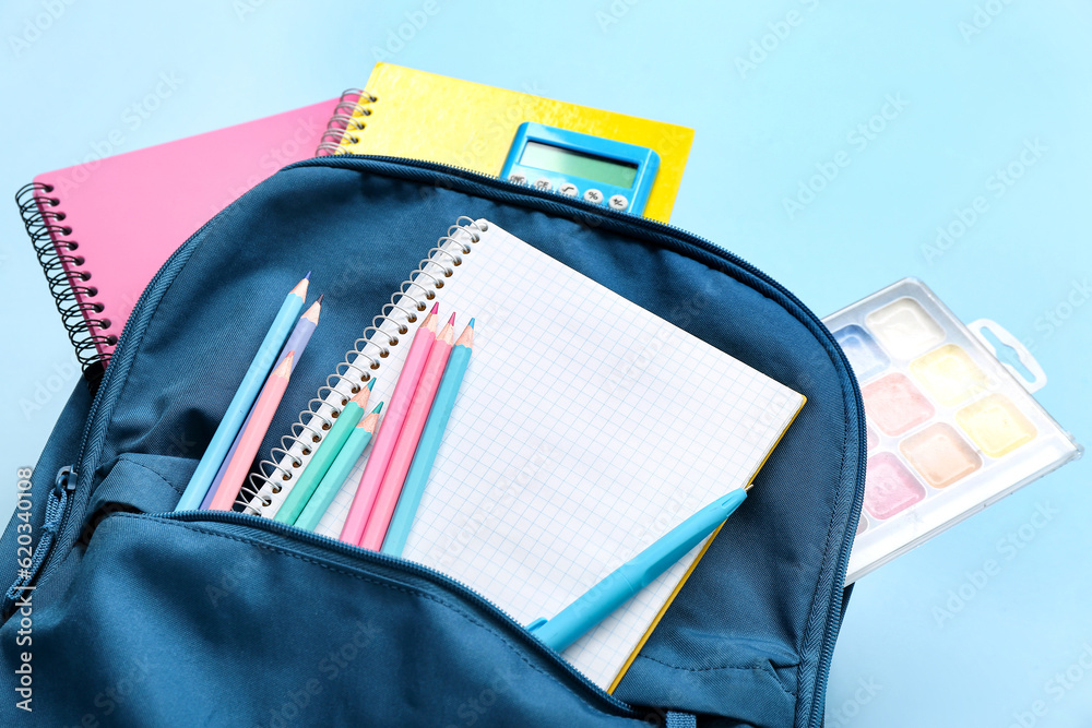 Backpack with blank notebook and stationery on blue background