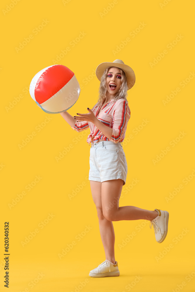 Young woman with beach ball on yellow background