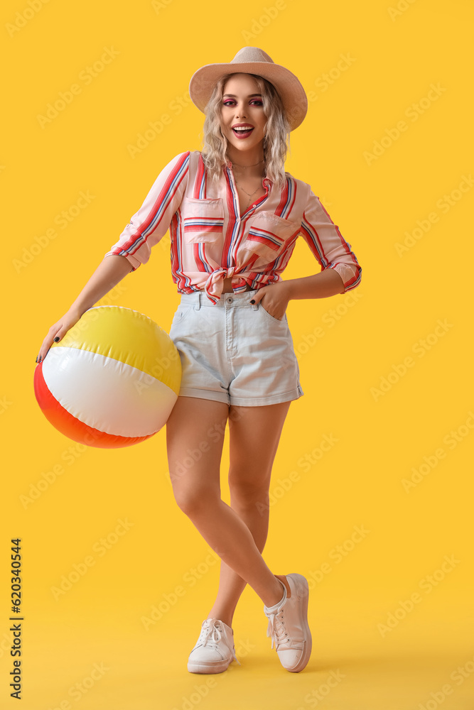 Young woman with beach ball on yellow background