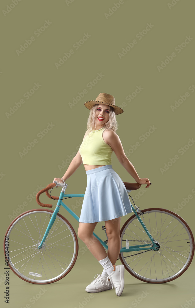 Young woman in summer hat with bicycle on green background