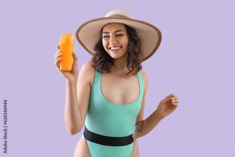 Young woman in swimsuit with sunscreen cream on lilac background