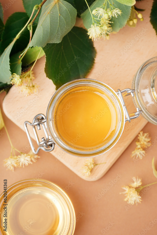 Wooden board with jar of linden honey on brown background