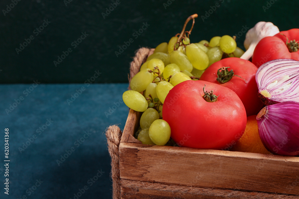 Wooden box with different fresh fruits and vegetables on green background, closeup