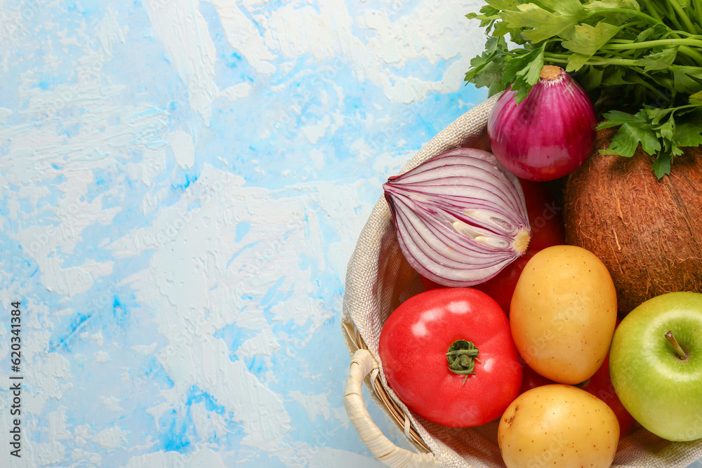 Wicker basket with different fresh fruits and vegetables on blue background, closeup