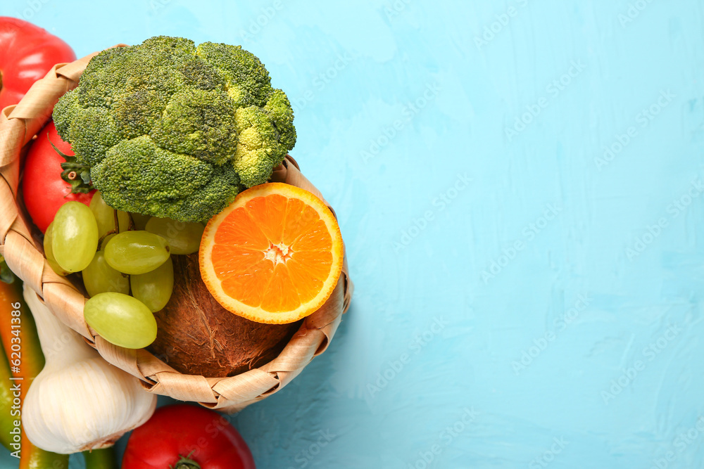 Wicker basket with different fresh fruits and vegetables on blue background, closeup