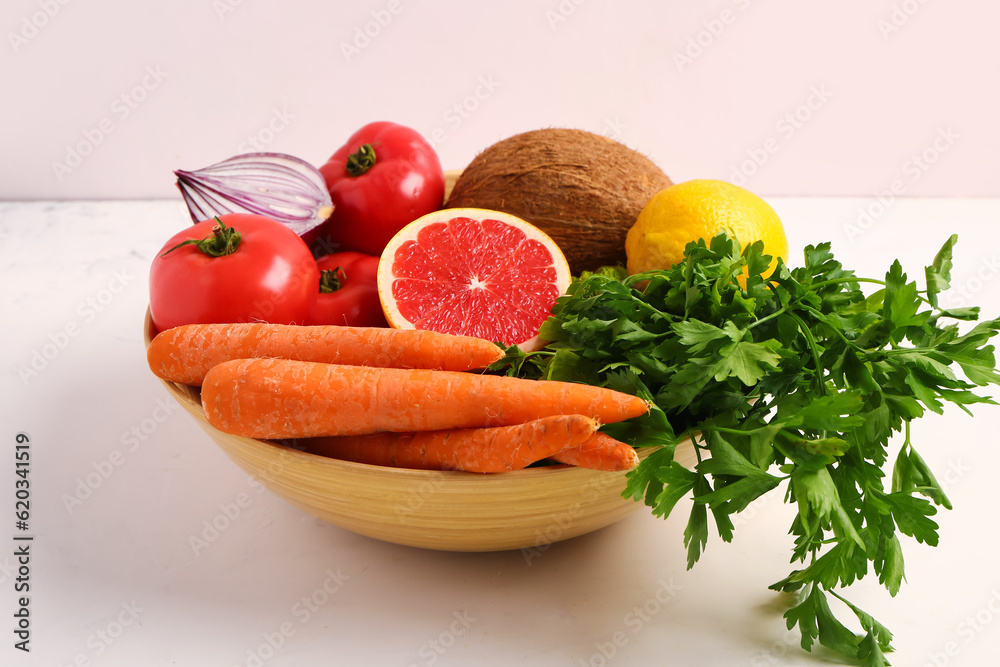 Bowl with different fresh fruits and vegetables on white table