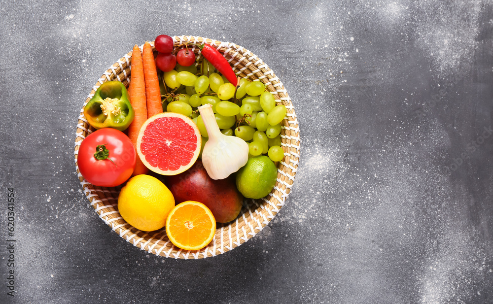 Wicker bowl with different fresh fruits and vegetables on grey background