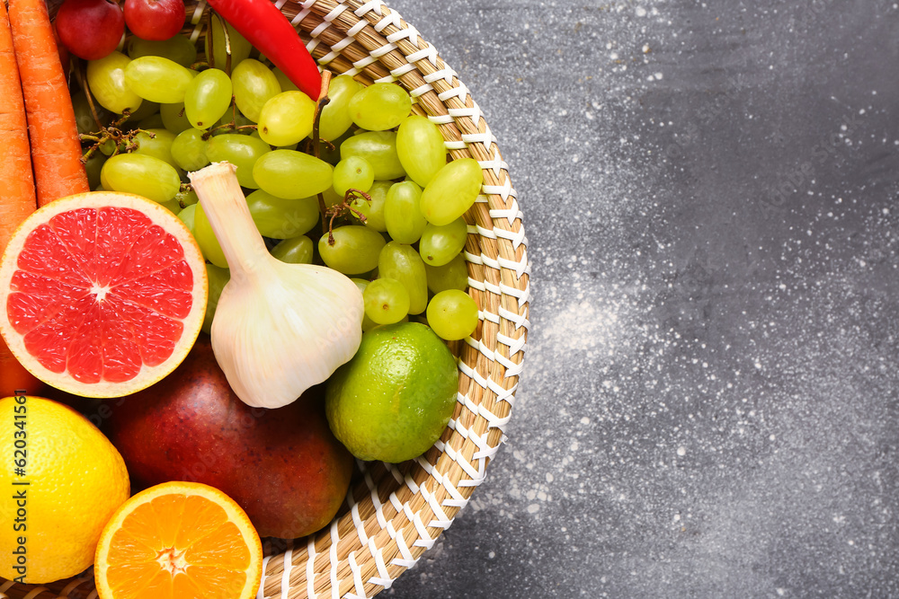 Wicker bowl with different fresh fruits and vegetables on grey background, closeup