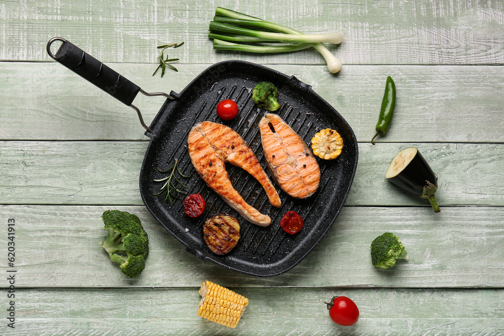 Frying pan with tasty grilled salmon steaks and vegetables on green wooden background