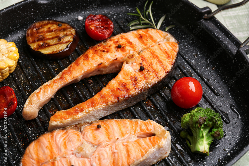 Frying pan with tasty grilled salmon steaks and vegetables on table