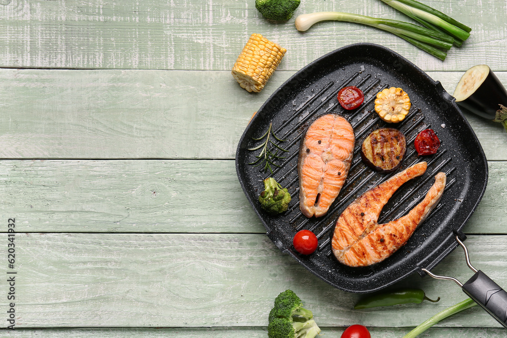 Frying pan with tasty grilled salmon steaks and vegetables on green wooden background