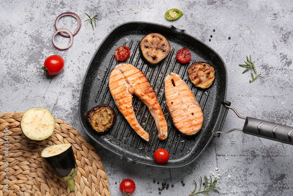 Frying pan with tasty grilled salmon steaks and vegetables on grey background