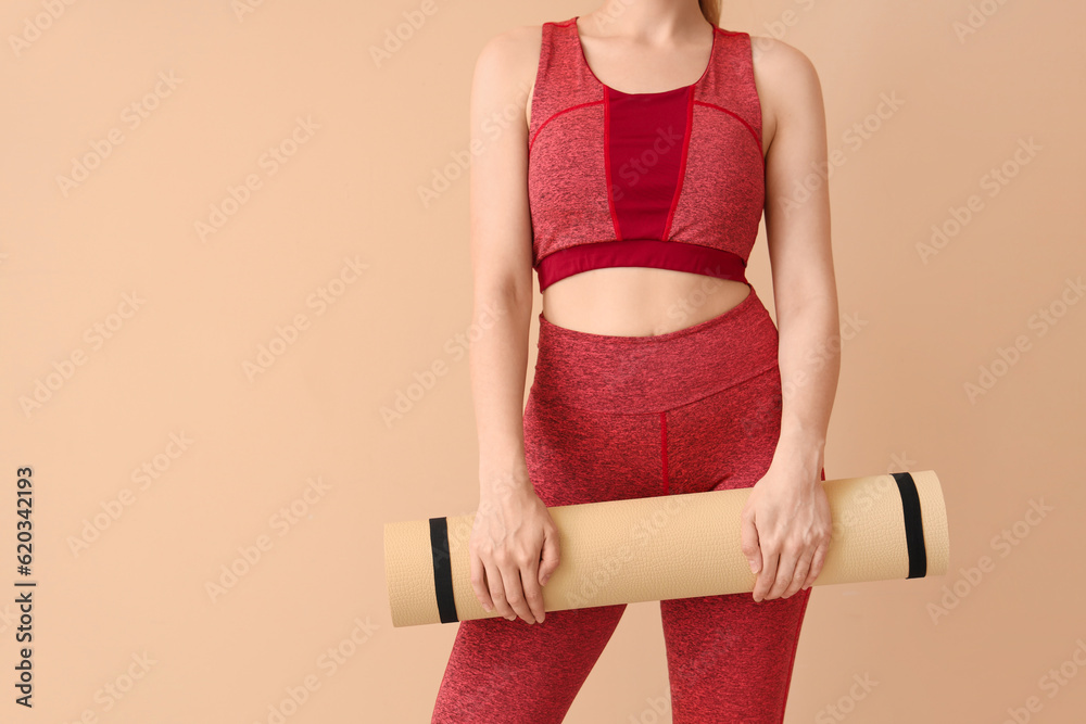 Young woman in sportswear and with yoga mat on beige background