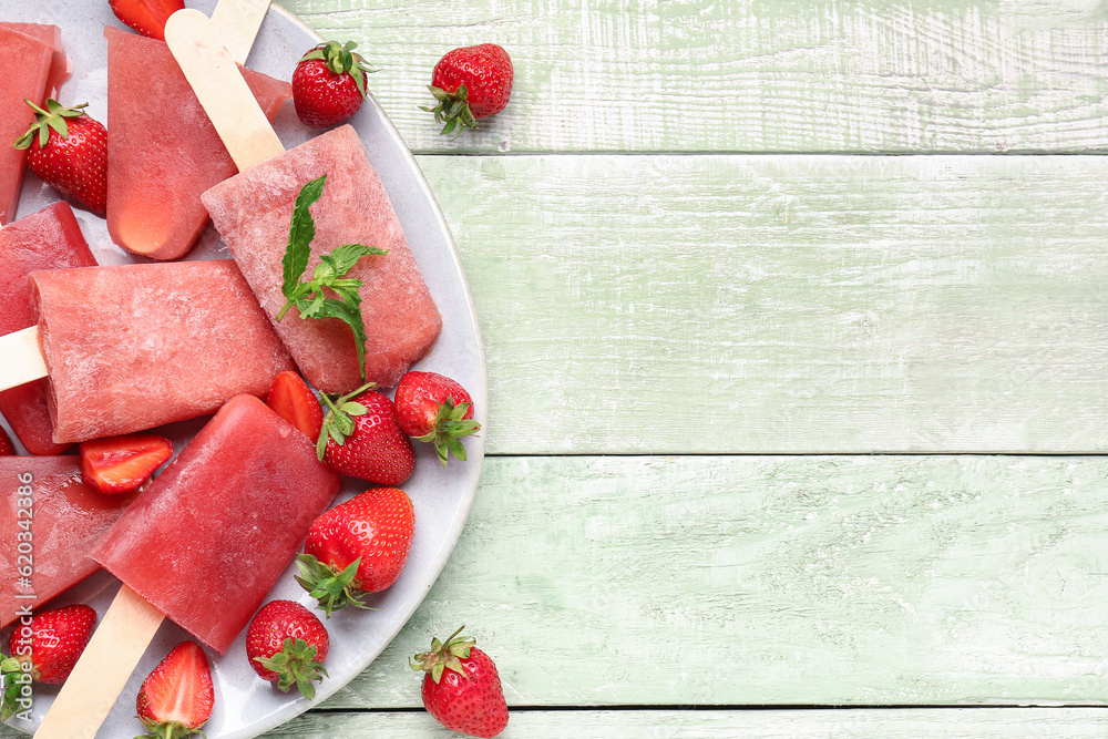 Plate with sweet strawberry ice-cream popsicles on green wooden background