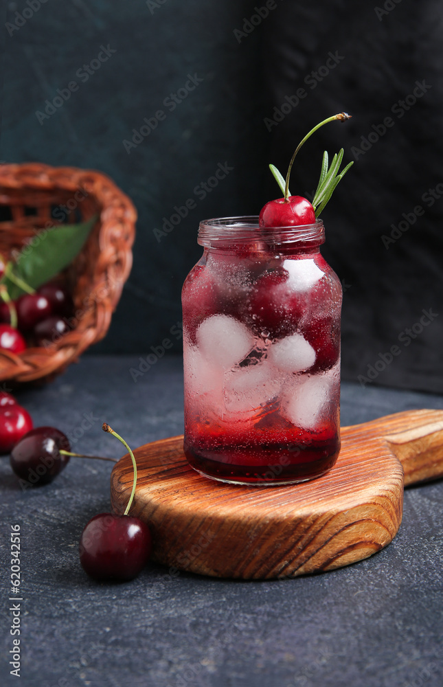 Wooden board with jar of tasty cherry lemonade and rosemary on dark background