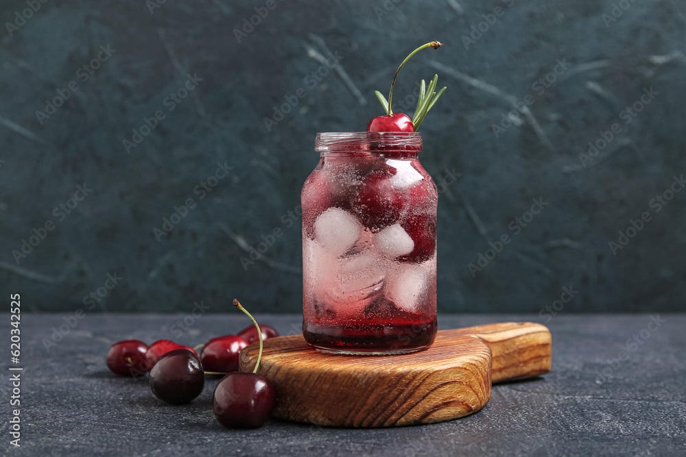 Wooden board with jar of tasty cherry lemonade and rosemary on dark background