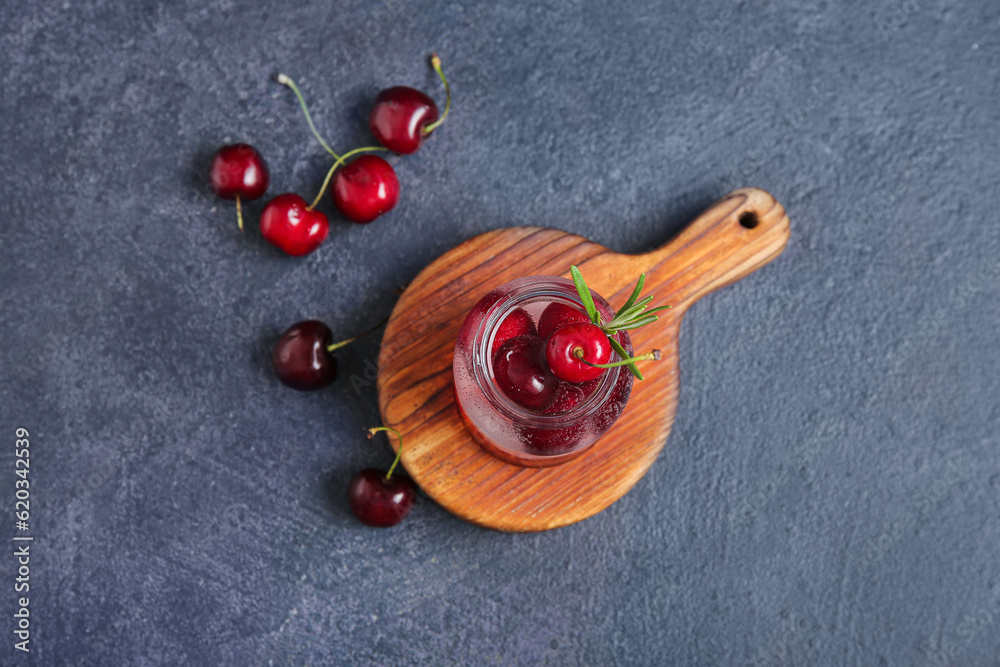 Wooden board with jar of tasty cherry lemonade and rosemary on dark background