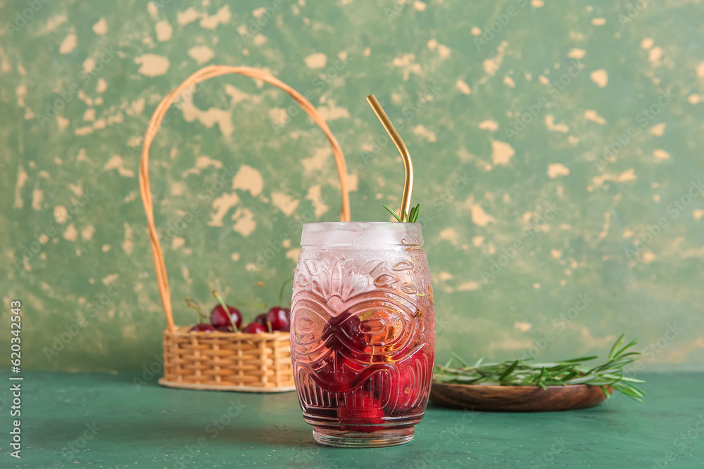 Glass of tasty cherry lemonade and plate with rosemary on green table