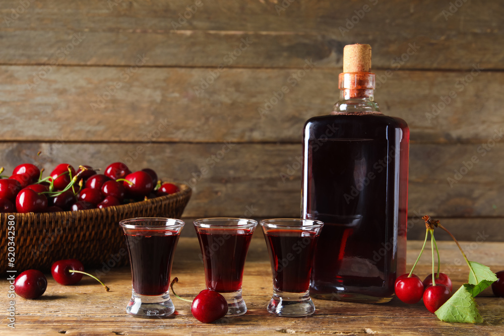 Shots and bottle with sweet cherry liqueur on wooden background