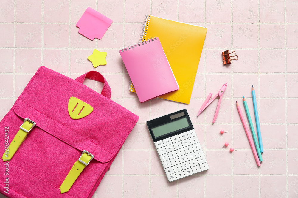 Pink school backpack with calculator, notebooks and pencils on light tile background