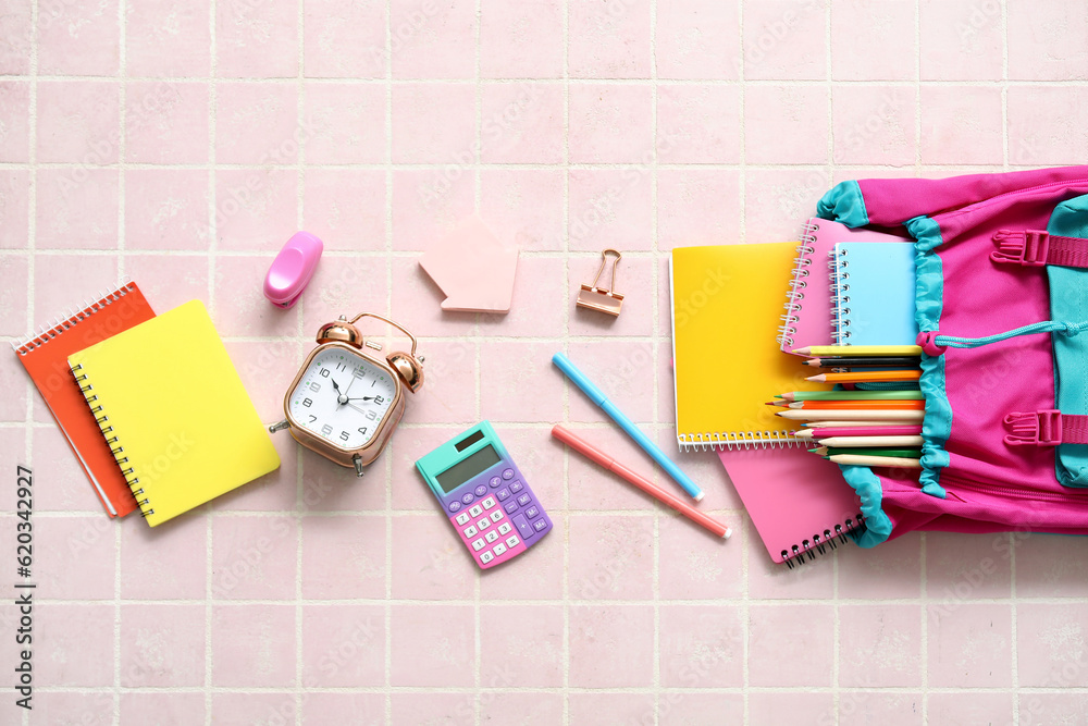 Colorful school backpack with notebooks, alarm clock and pencils on pink tile background