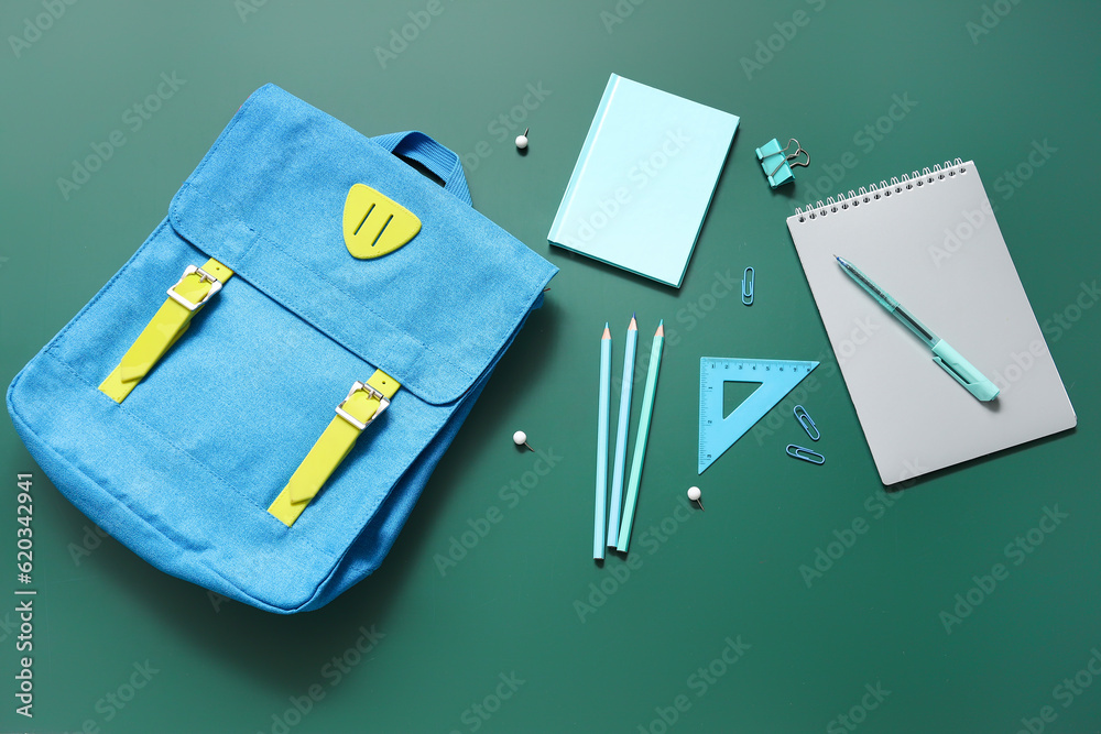 Blue school backpack with notebooks, paper clips and pencils on green background