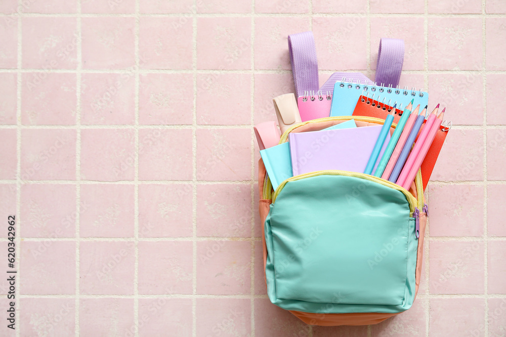 Colorful school backpack with notebooks, pencils and markers on pink tile background