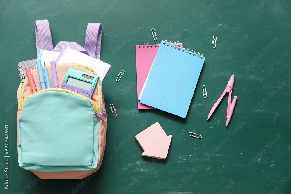 Colorful school backpack with notebooks, calculator and compass on green background