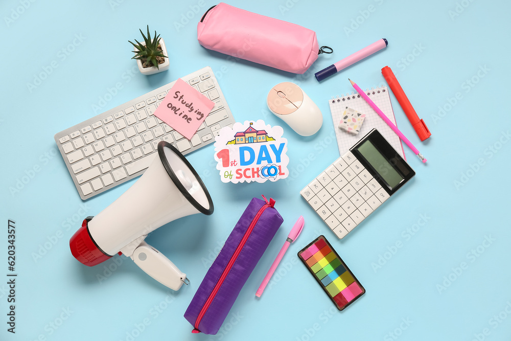 Stationery, keyboard, megaphone and sheet with text 1ST DAY OF SCHOOL on blue background