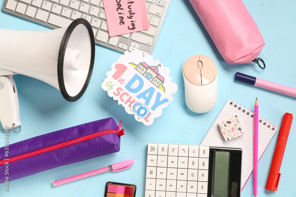 Stationery, keyboard, megaphone and sheet with text 1ST DAY OF SCHOOL on blue background