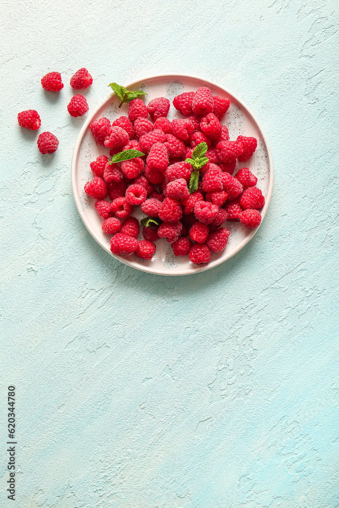 Plate with fresh raspberries and mint on light blue background