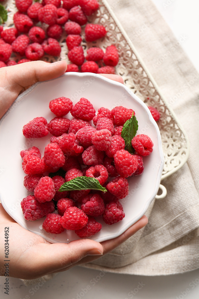 Female hands holding plate with fresh raspberries and mint, closeup