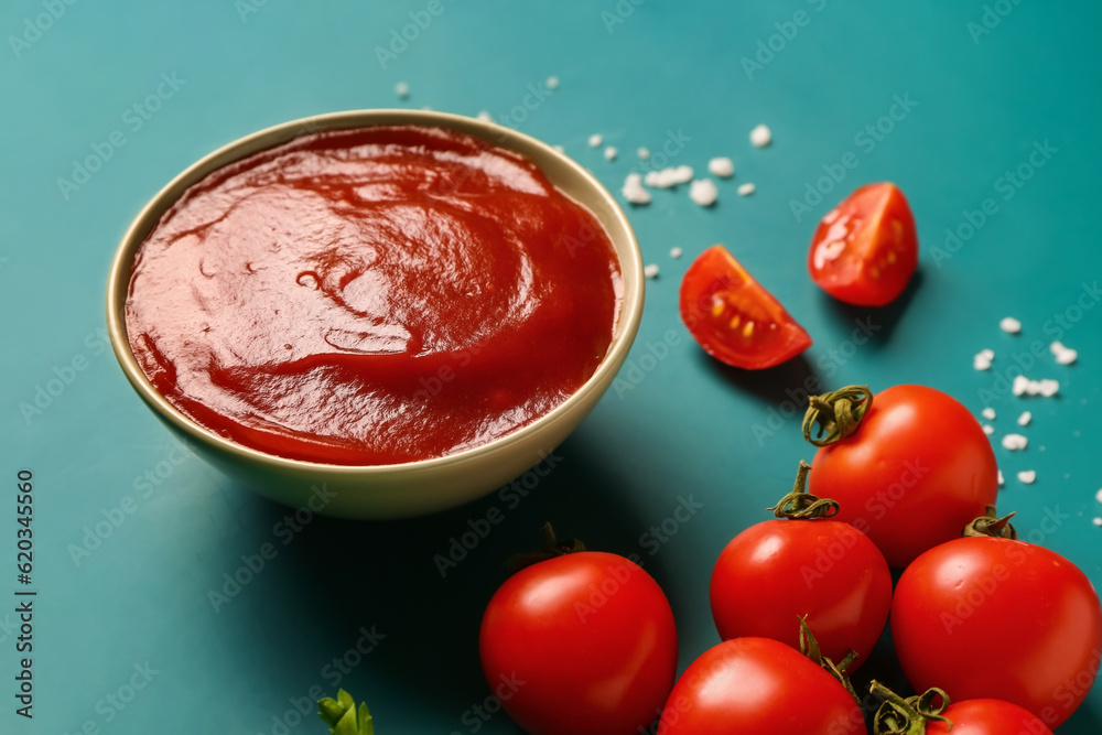 Bowl with tomato paste and fresh vegetables on blue background