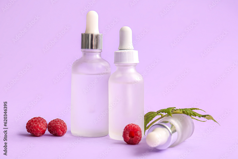 Bottles of cosmetic raspberry oil on lilac background