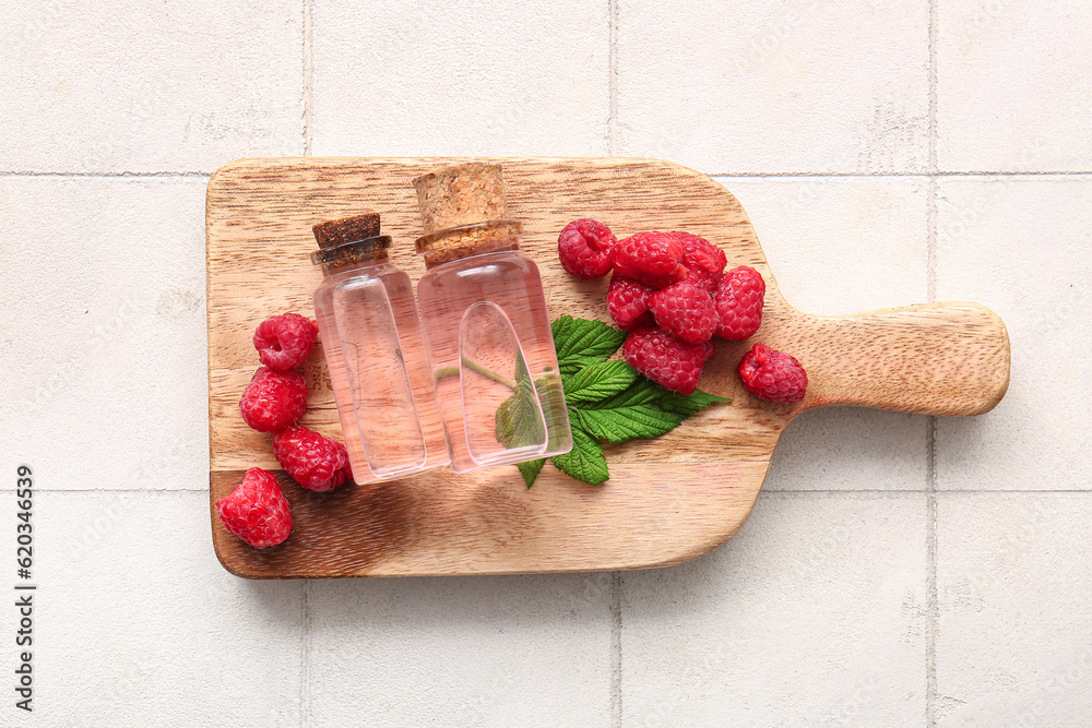 Wooden board with bottles of cosmetic raspberry oil on white tile background