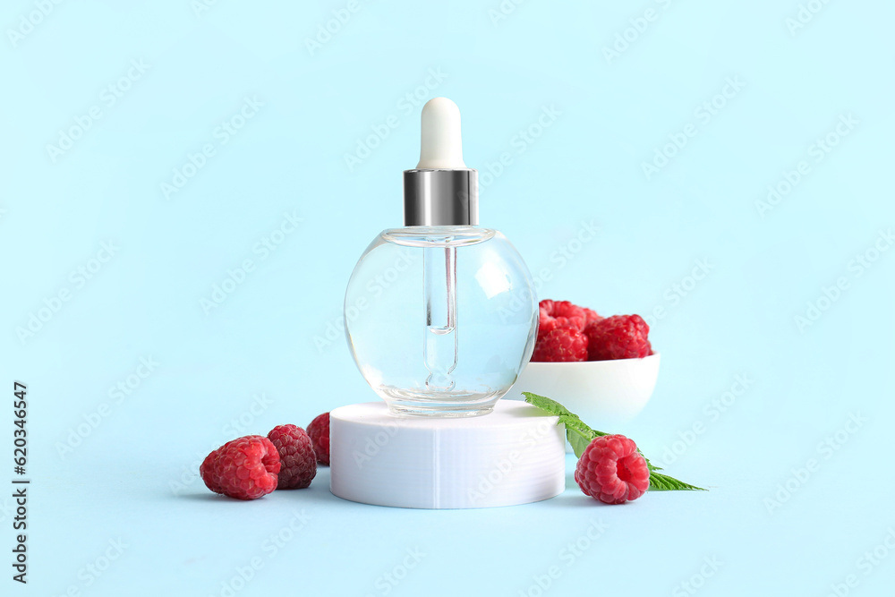 Decorative podium with bottle of cosmetic raspberry oil on blue background