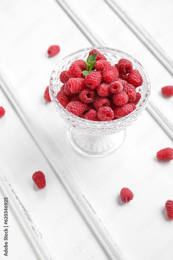 Glass bowl with fresh raspberry on light wooden background