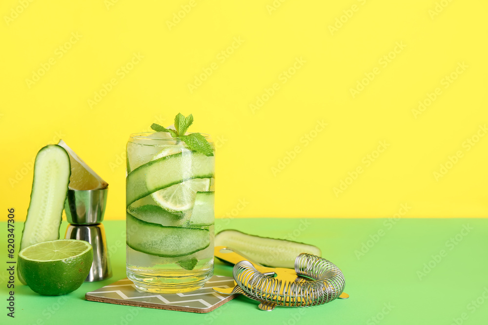 Glass of cucumber mojito with bartender tools on color background