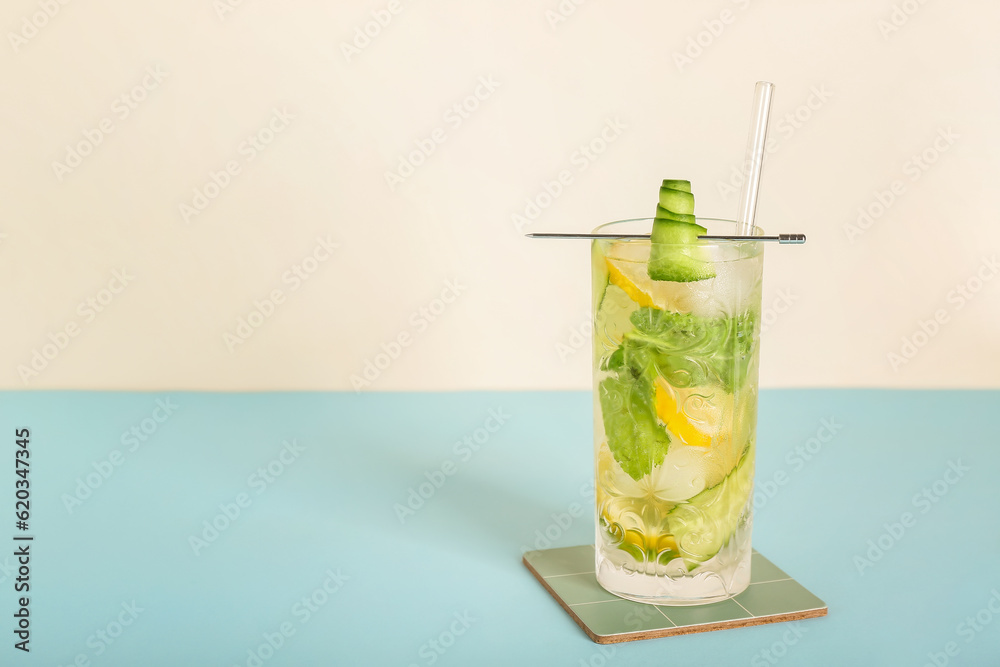 Glass of mojito with lemon, cucumber and ice cubes on blue table near white wall