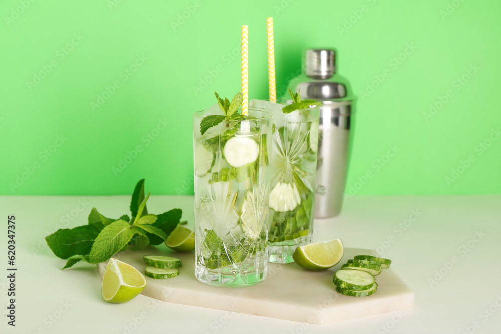 Glasses of mojito cocktails with cucumber, lime and mint on green background