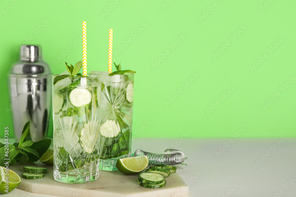 Glasses of cucumber mojito cocktails with bartender tools on green background