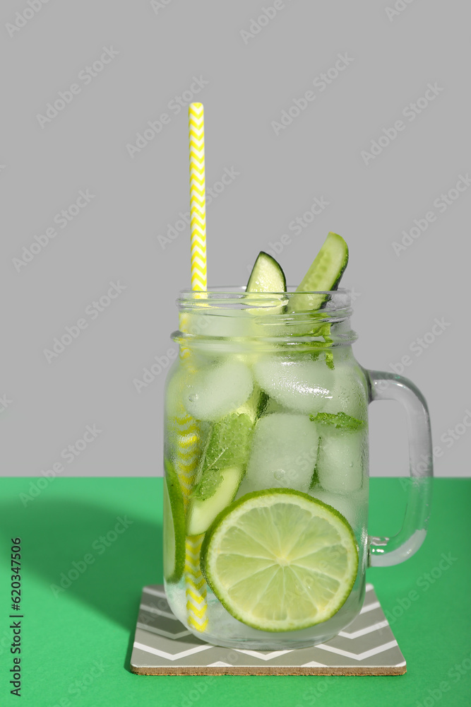 Mojito cocktail with cucumber, lime and ice in glass jar on green background