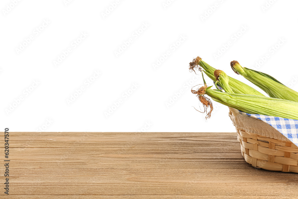 Wicker basket with fresh corn cobs on wooden table against white background