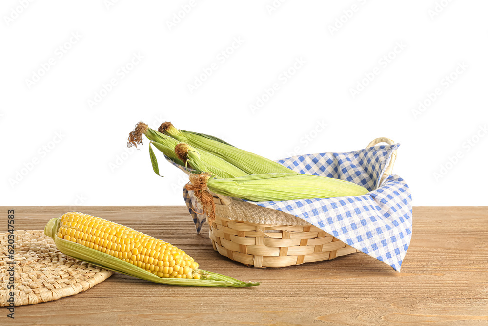 Wicker basket with fresh corn cobs on wooden table against white background