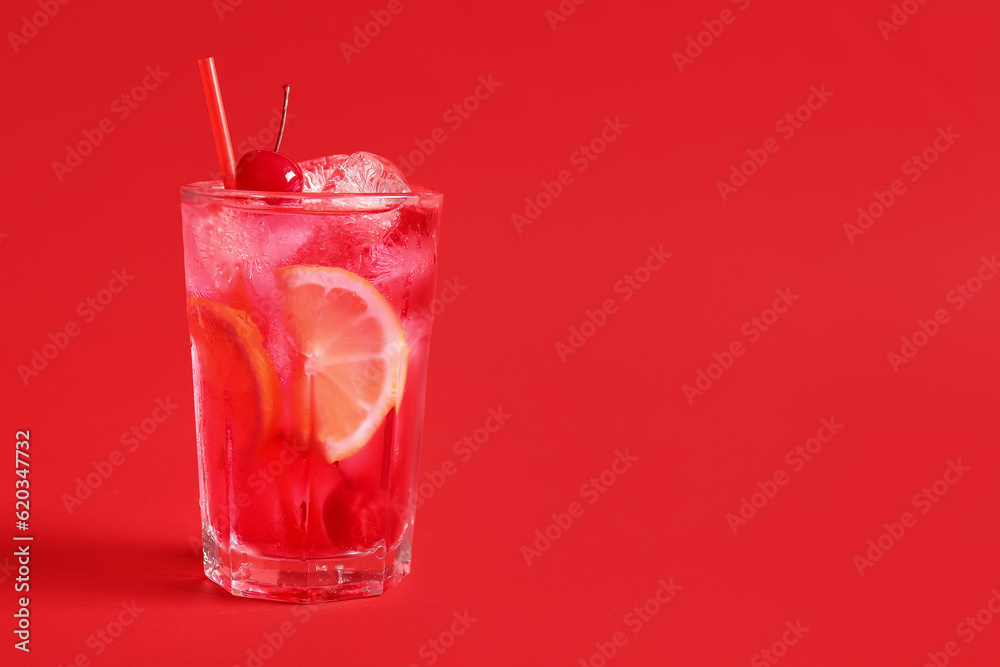 Glass of tasty cocktail with maraschino cherry on red background