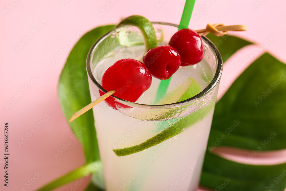 Glass of tasty cocktail with maraschino cherries on pink background