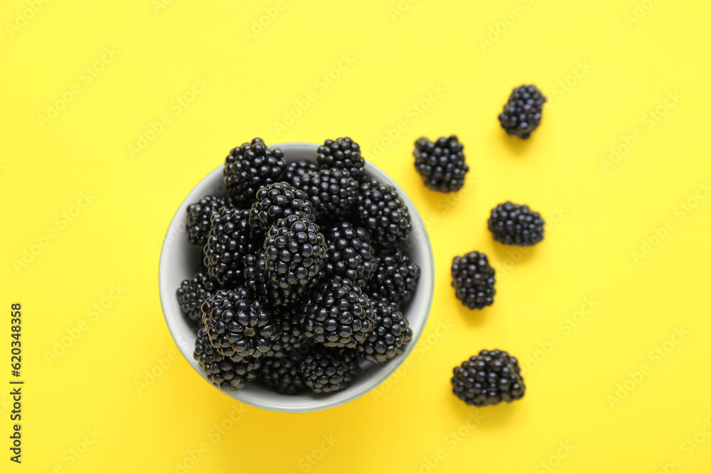 Bowl with fresh blackberry on yellow background, closeup